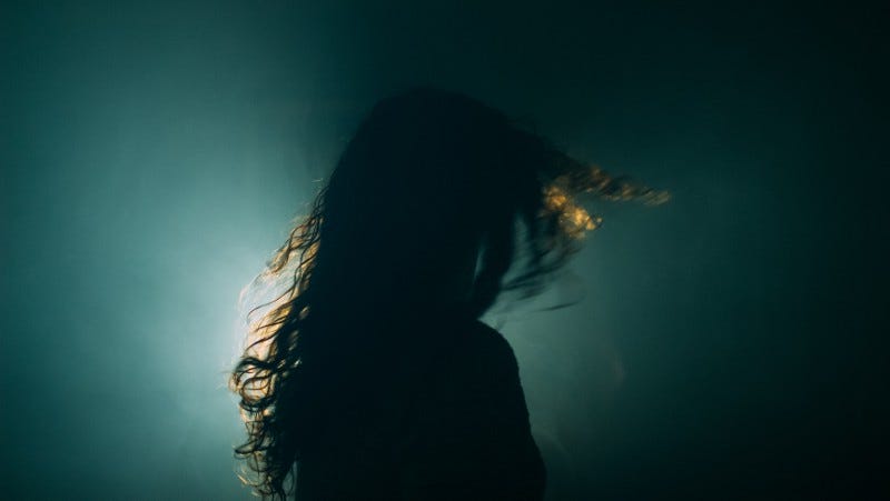 A dark photo of a rear view of a woman turning her head.