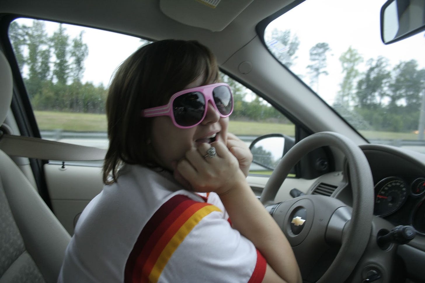 An old pic of Deanna behind the wheel of a chevy wearing pink aviators and a white tshirt with stripes. She's ready for a road trip. But not to sell Mary Kay. 