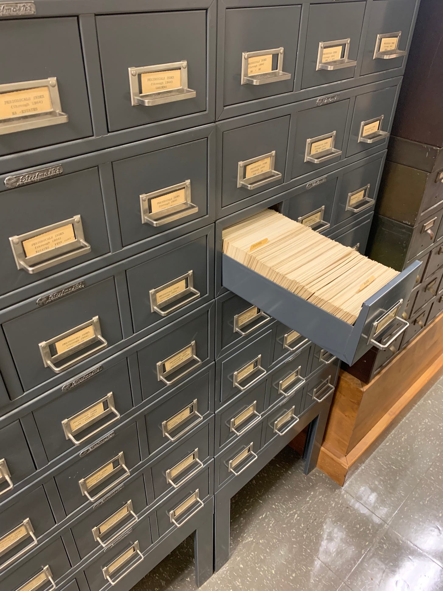 A gray metal cabinet with yellowed labels on the drawer fronts. One drawer is pulled open, and has numerous index cards inside.