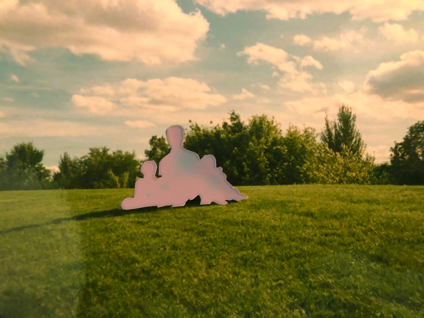 grassy field with blue skies and fluffy clouds. cut out silhouette of three people sitting together. 