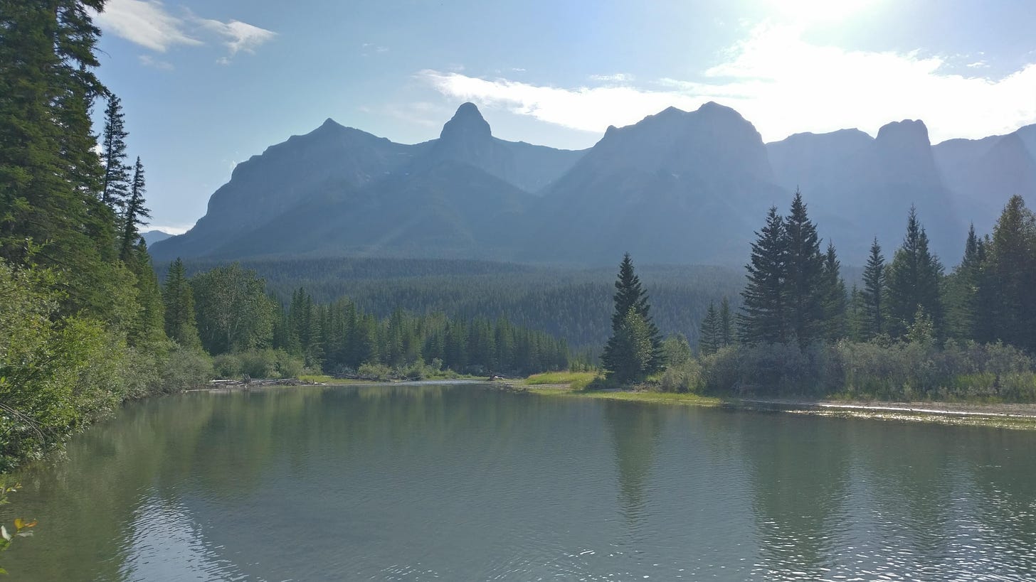 A picture of Canmore, taken from the side of a river with mountains visible in the hazy distance