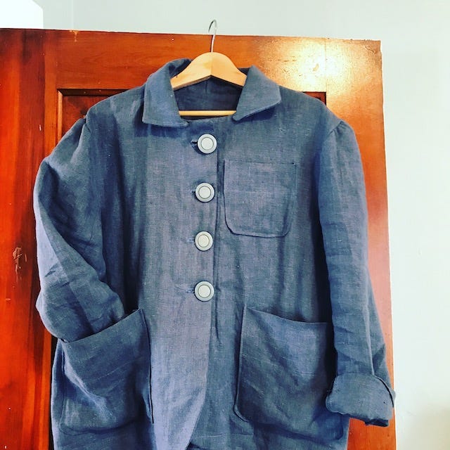 Blue linen jacket with three pockets, hanging on a door. 