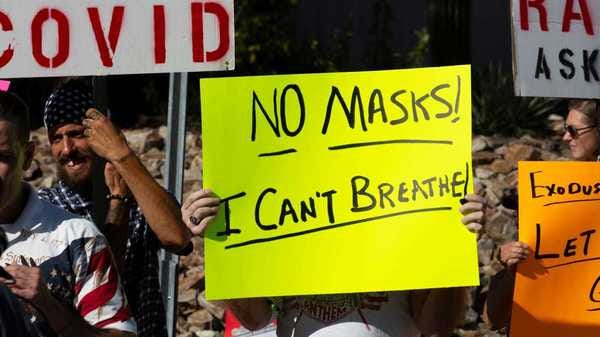 A white protester in an anti-healthcare protest holds a sign that reads "No Masks: I Can't Breathe"