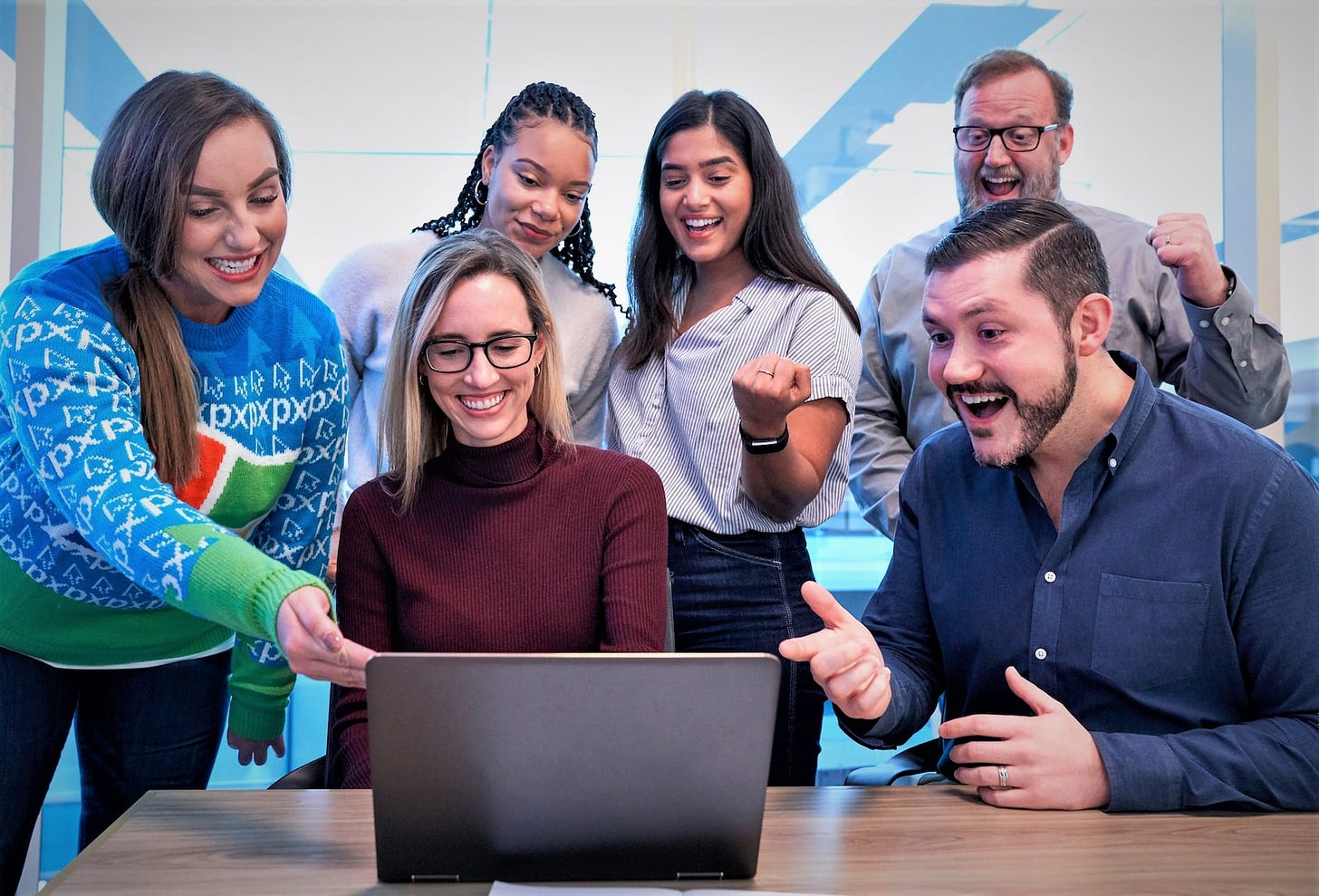 group of happy excited people gathered around a computer screen