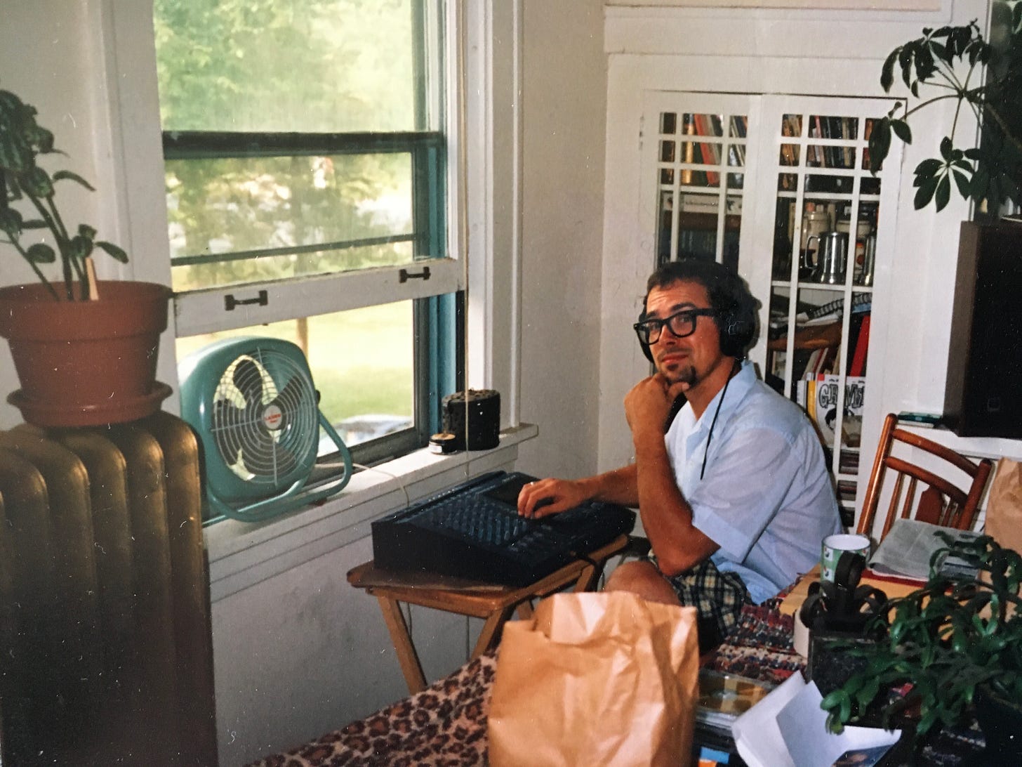 The artist Faux Jean seated with 4 track recording device in front of a window overlooking Knox Ave. in Minneapolis.