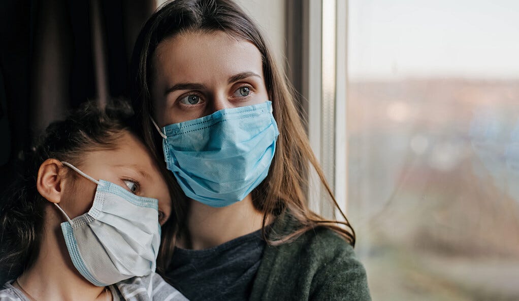 Mother and daughter wearing face mask looking out a window.