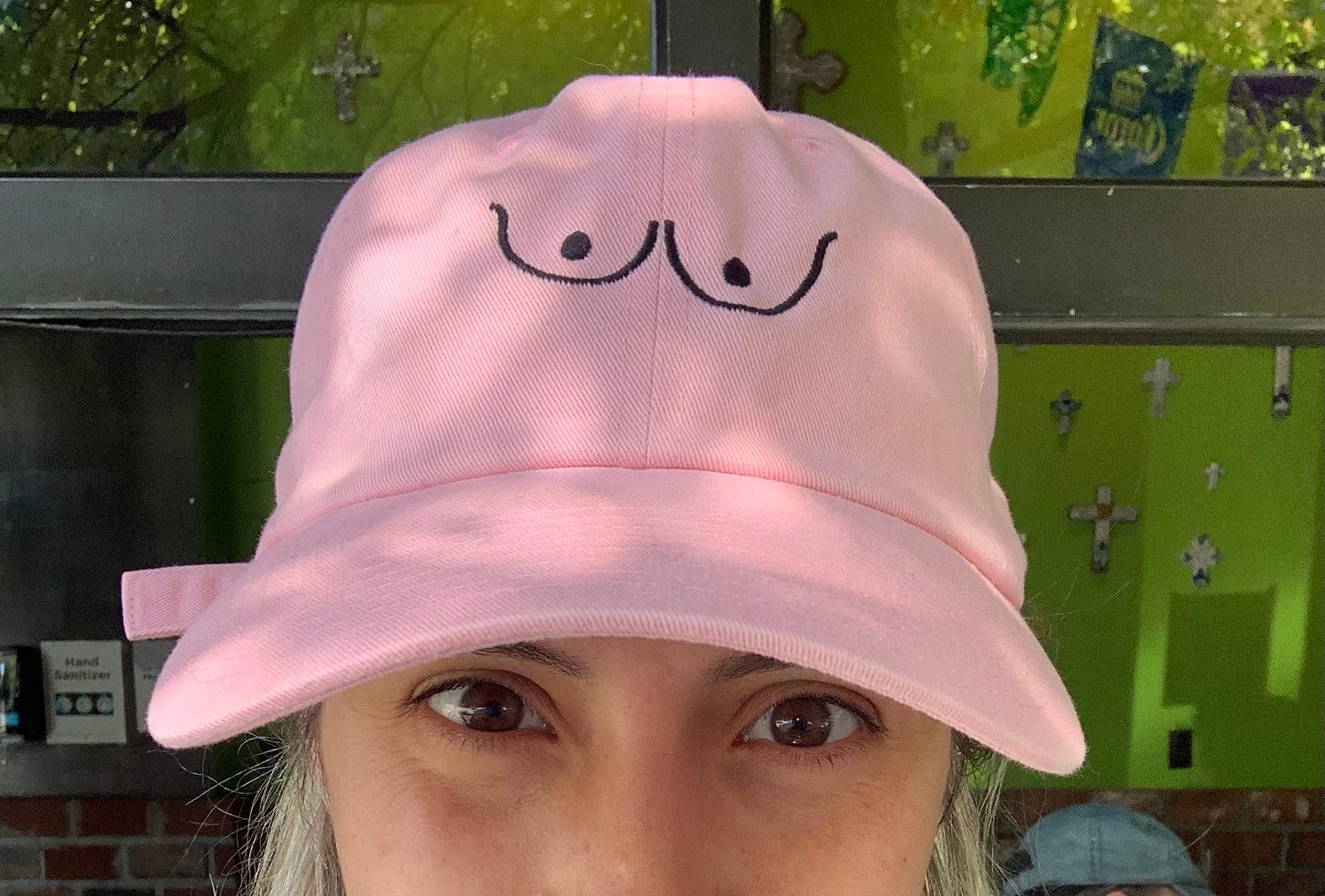 A blonde, white woman wears a millennial pink cap with the black outline of two breasts on it