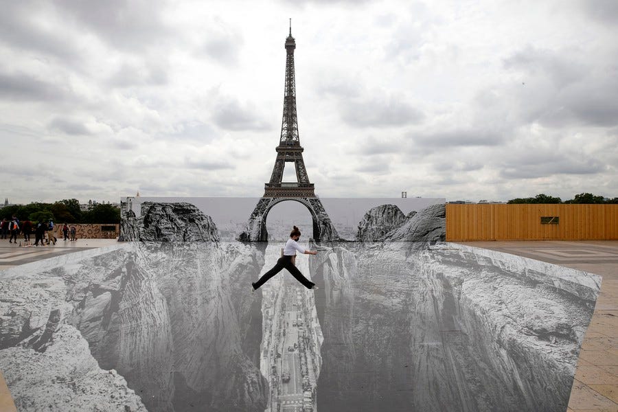 A woman jumps across a "gap in a large optical-illusion artwork set up in front of the Eiffel Tower.