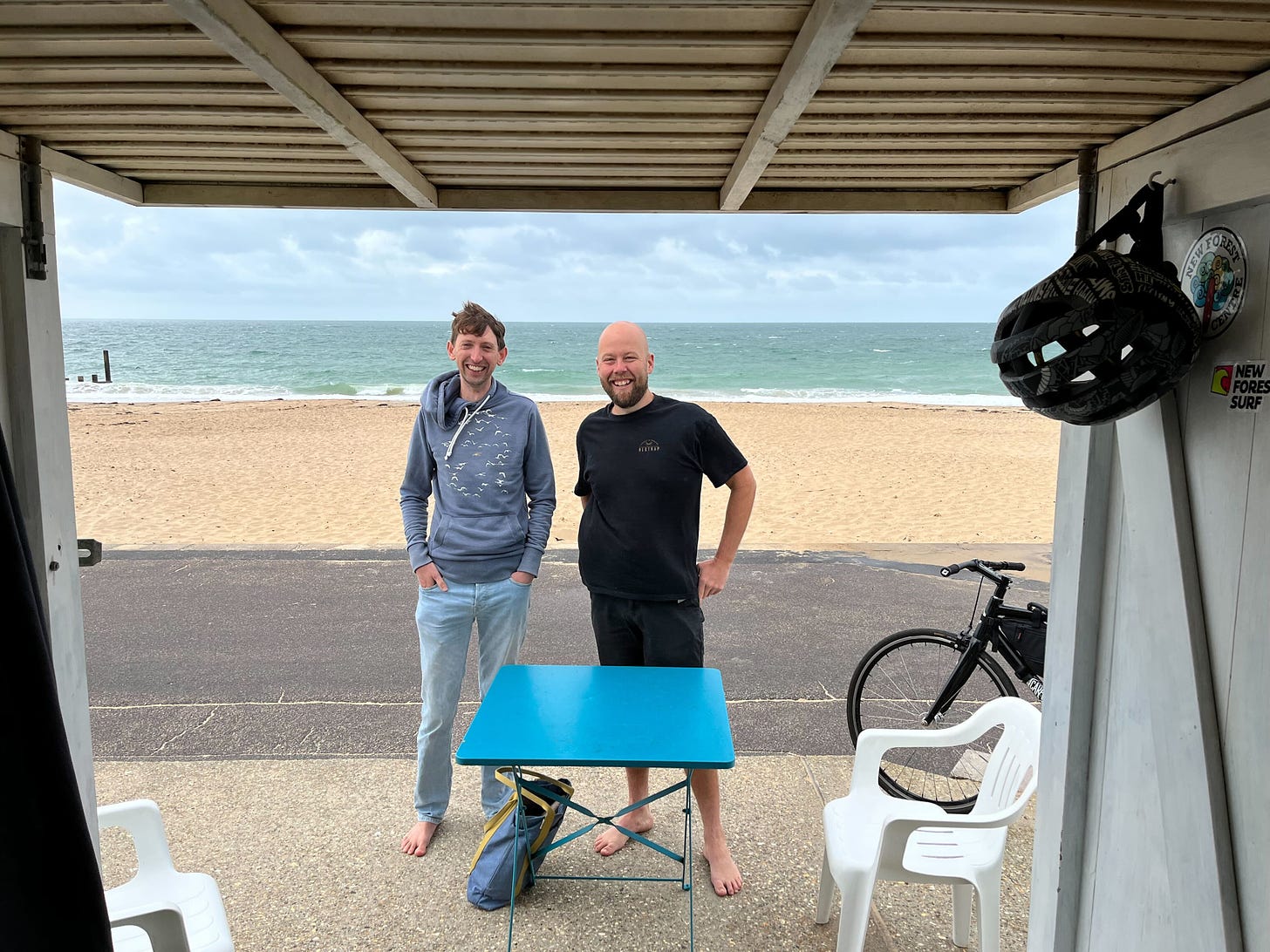 Nick and Tom standing in front of a beach hut with the sea behind them