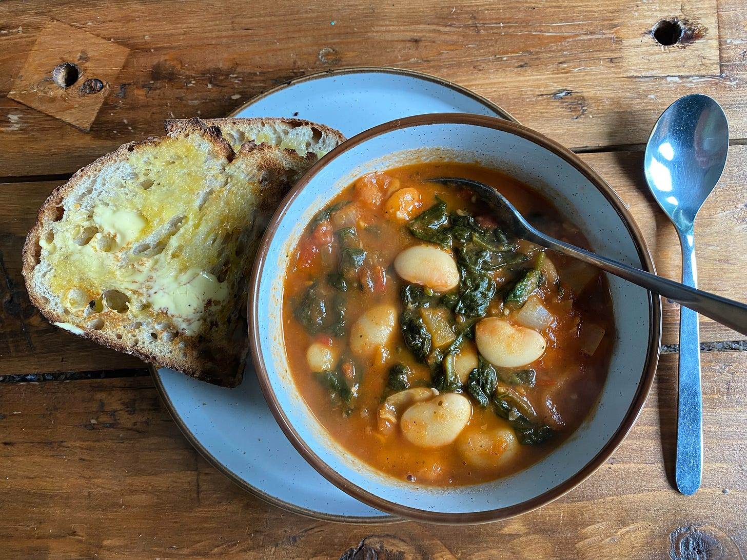 Bowl of soup with beans, green vegetables and a tomato broth in a bowl, a piece of bread and butter to the side