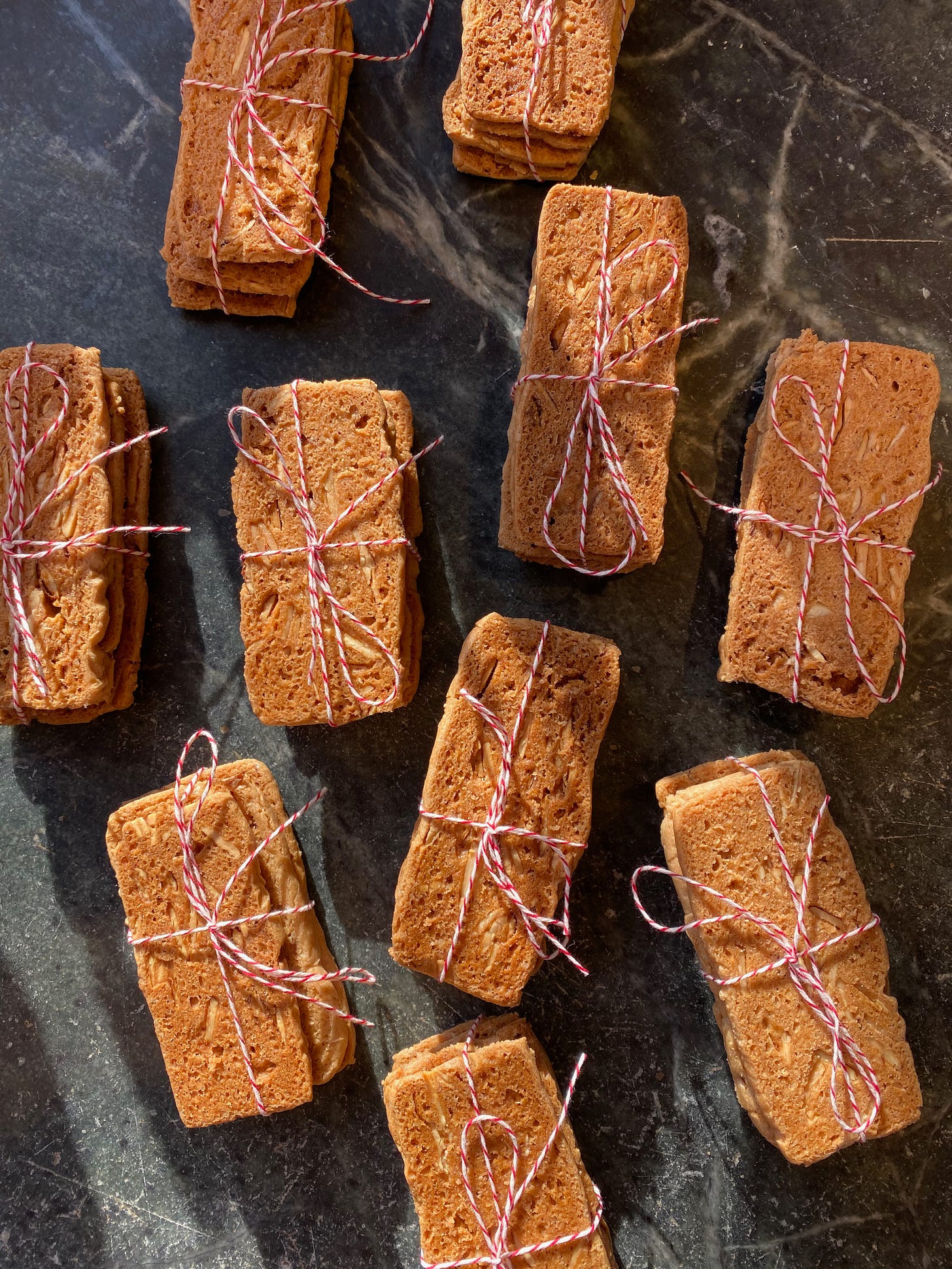 Several small bundles of thin rectangular cookies tied up with red and white baker’s twine sit on a stone counter.