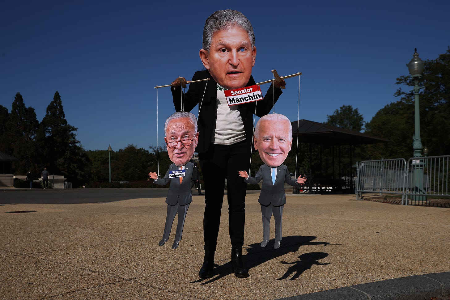 WASHINGTON, DC - OCTOBER 20: A demonstrator wears a photograph of Sen. Joe Manchin (D-WV) as a mask while playing a puppet-master at the periphery of a rally highlighting the efforts of Congressional Democrats to legislate against climate change outside the U.S. Capitol on October 20, 2021 in Washington, DC. Organized by the League of Conservation Voters, the event hosted Democratic members of both the House of Representatives and the Senate. (Photo by Chip Somodevilla/Getty Images)