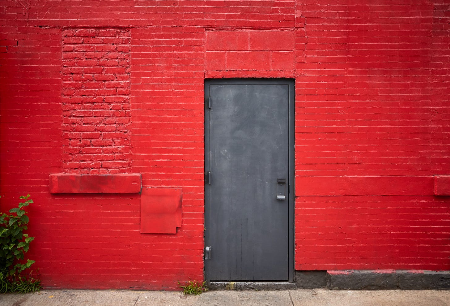 A dark door stands closed in a bright red brick wall.