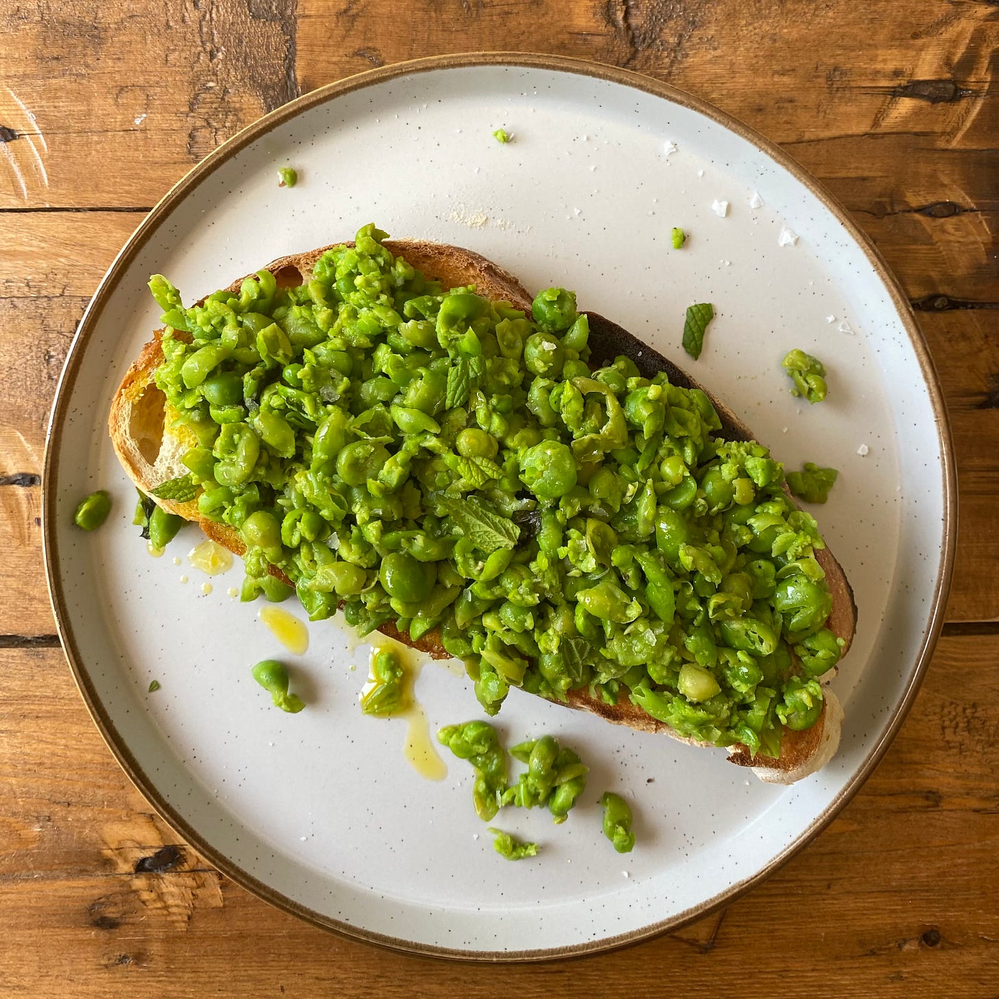 slice of toast topped with smashed peas drizzled with oil and torn mint leaves