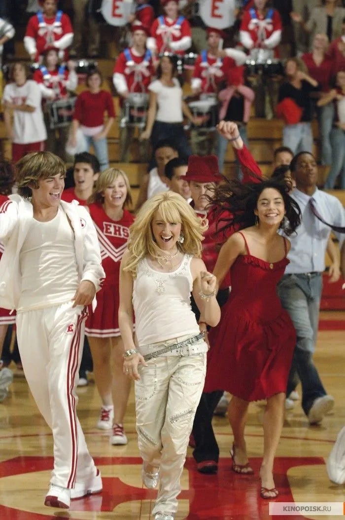 Sharpay Evans sings We're All In This Together in High School Musical (2006), flanked by Troy on her right and Gabriella on her left. They're all laughing and dancing in the basketball court along with the entire cast.