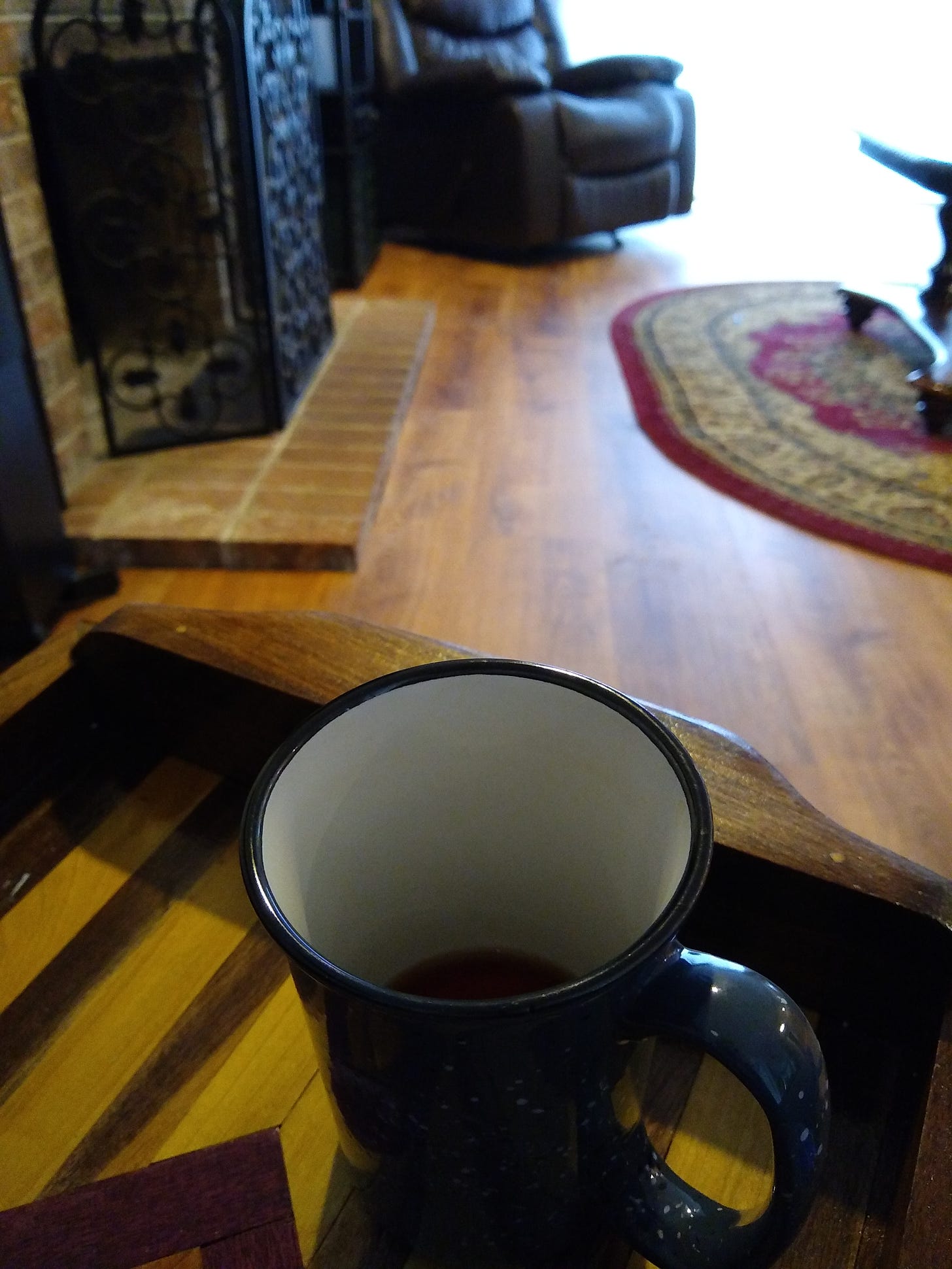 An almost empty mug of tea on a wooden tray, in a room with a fireplace, wood floor, area rug