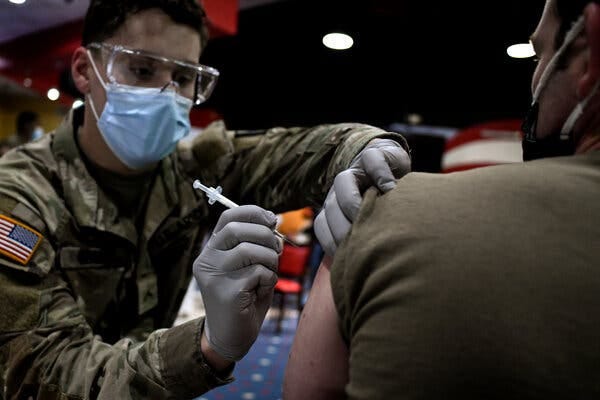A member of the military receiving a vaccine from a service member wearing a mask and safety glasses.