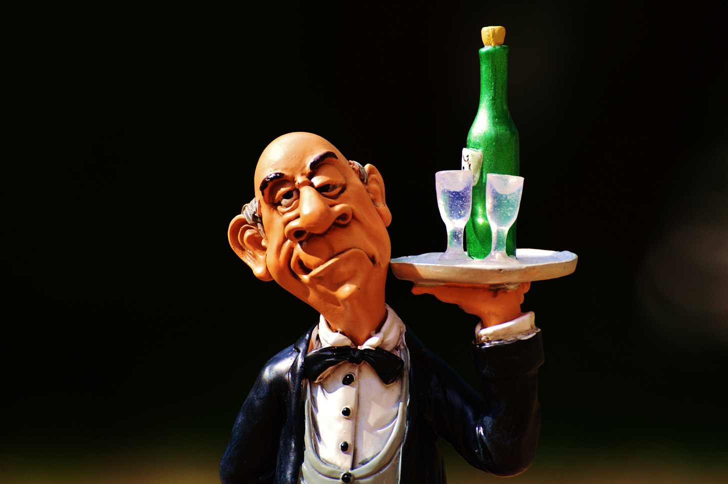 A ceramic butler sculpture with exagerated facial features that seem lopsided. He's carrying a tray of drinks.