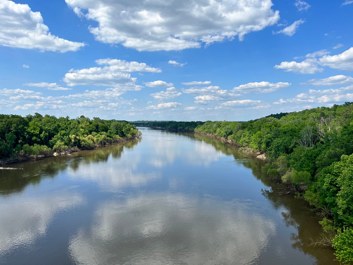 Photo of the Alabama River with blue sky and some clouds reflected in the water