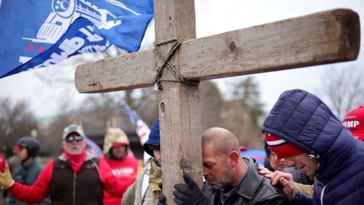 Supporters of President Donald Trump pray outside the U.S. Capitol on January 6, leaning on a large wooden cross.