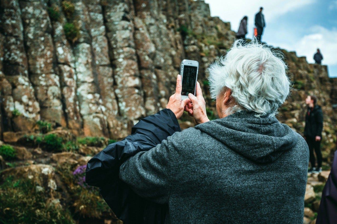Elder man in a grey hoodie shoot a photo of a cliff with his smartphone.
