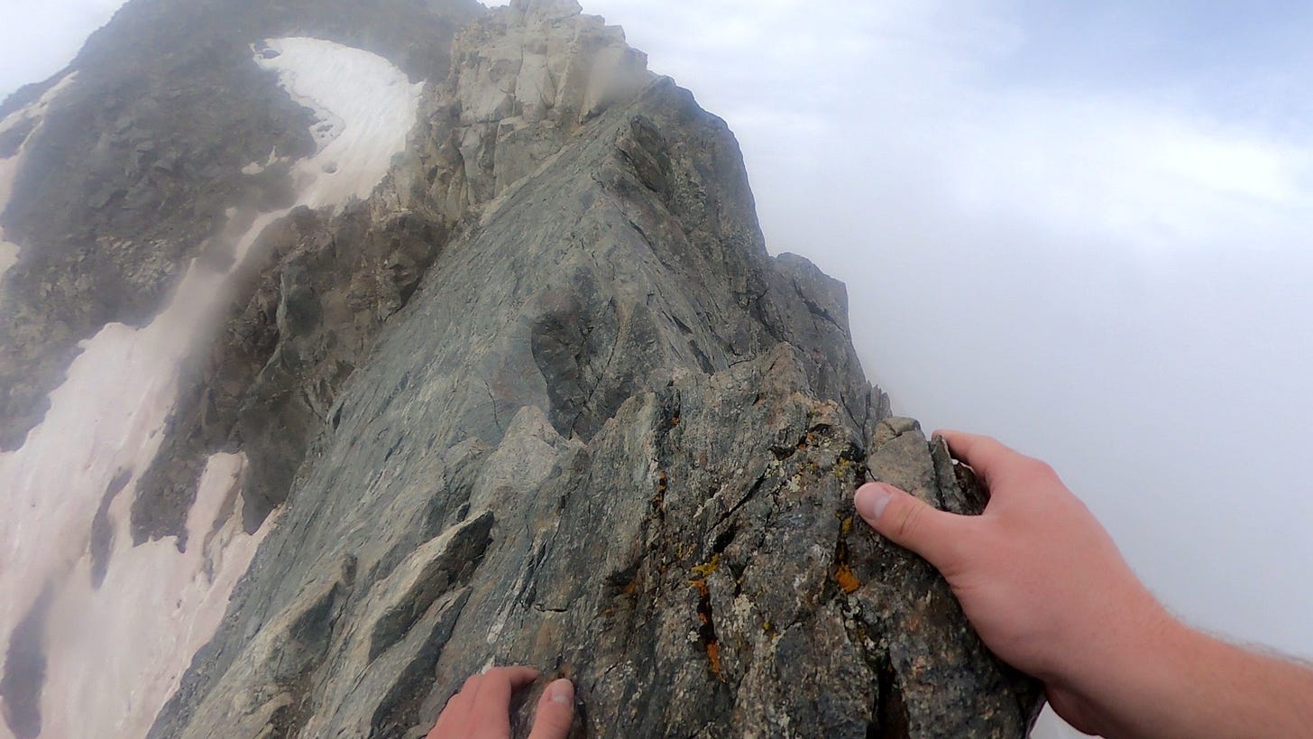 A point-of-view scramble up Kelso ridge. The craggy "knife's edge" traverse splits the frame in half. To the left: a steep and rocky drop. To the right: nothing but clouds.