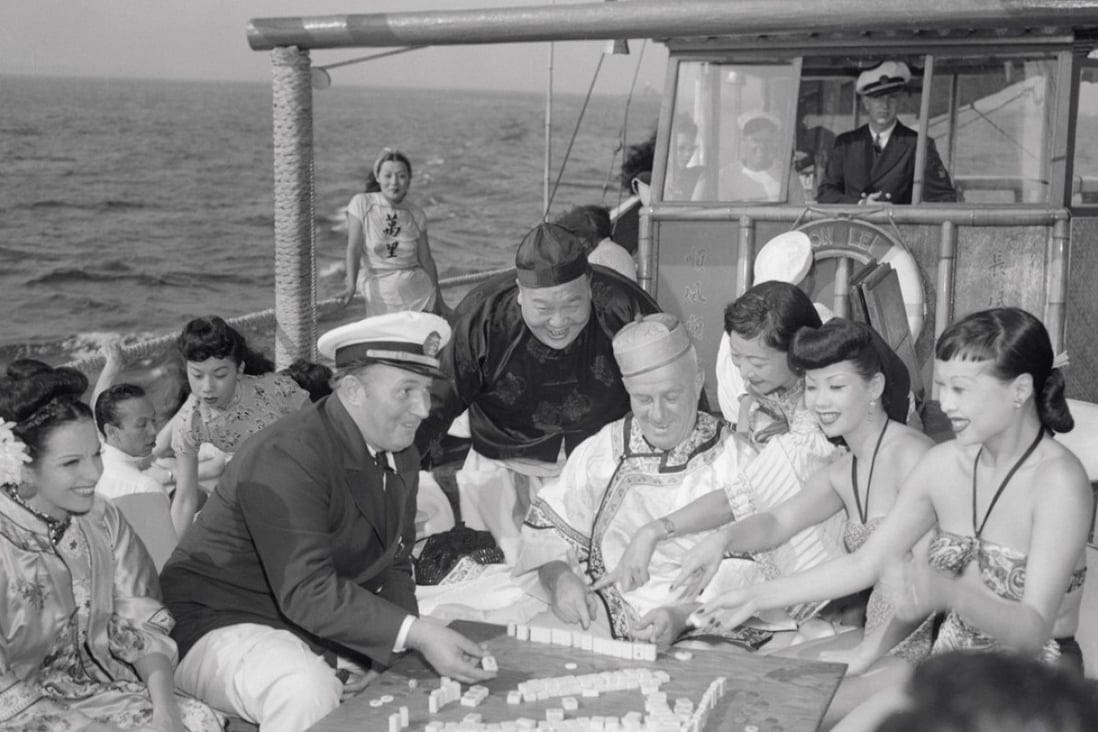 a group of people play mahjong aboard the Chinese junk Mon Lei, some in Chinese dress, all with amused faces