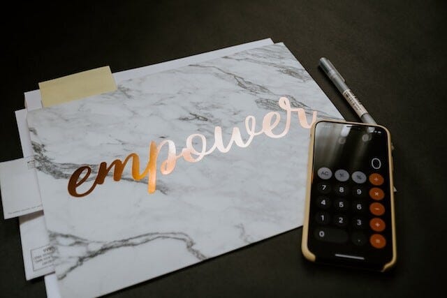 Calligraphed sign reading, “Empower”​ next to black mobile phone.