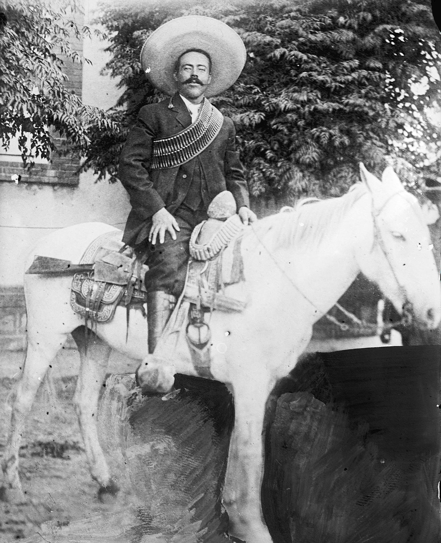 Man on horse wearing sombrero and ammo belt, gun on saddle