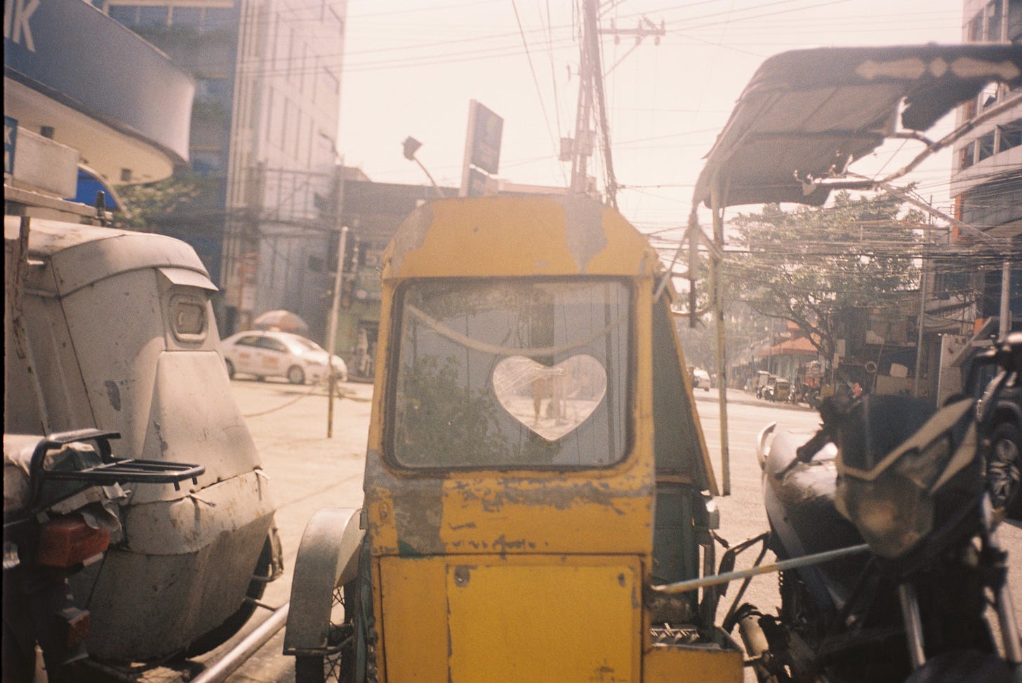 Street photo of a yellow tricycle with a heart-shaped cutout in the back window.