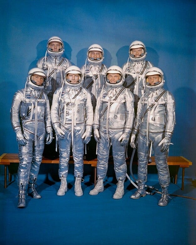 Official photo of the Mercury Seven. They are pictured in their silver astronaut suits.
