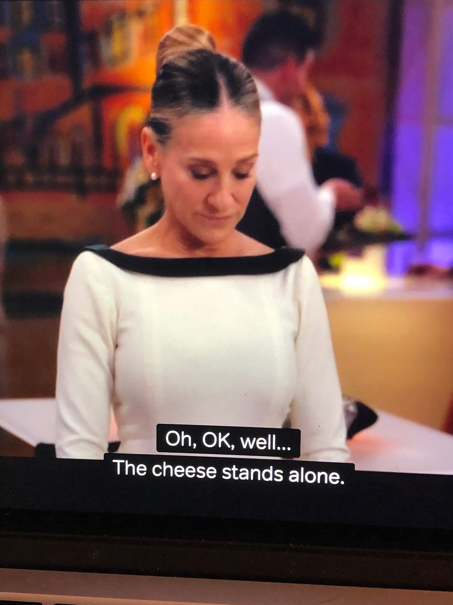 A still from 'And Just Like That' of a white middle aged woman with her eyes cast down. The Captions reads 'Oh, OK, well...The cheese stands alone.'