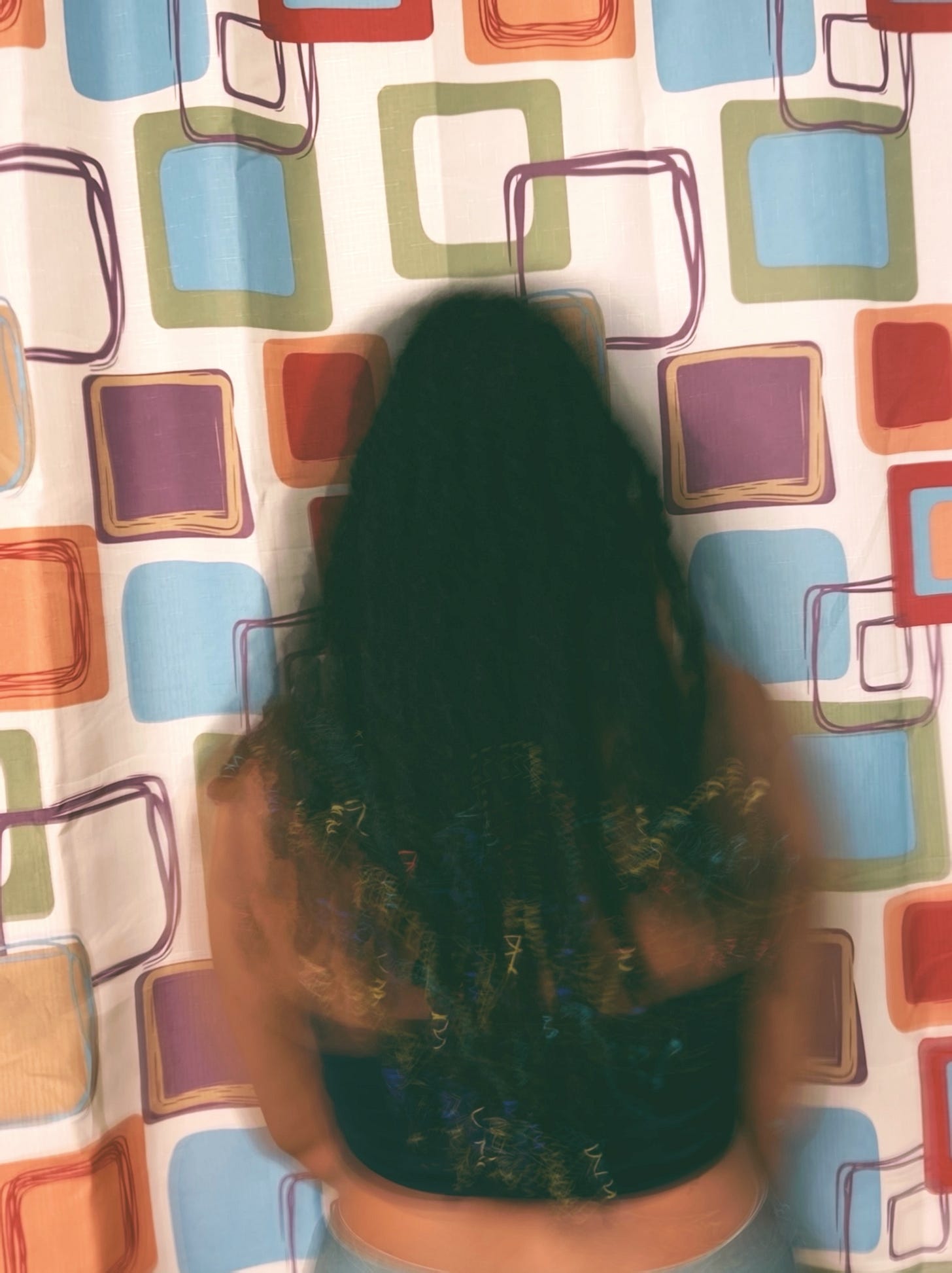 long exposure portrait of a black femme (me) in front of a patterned curtain 