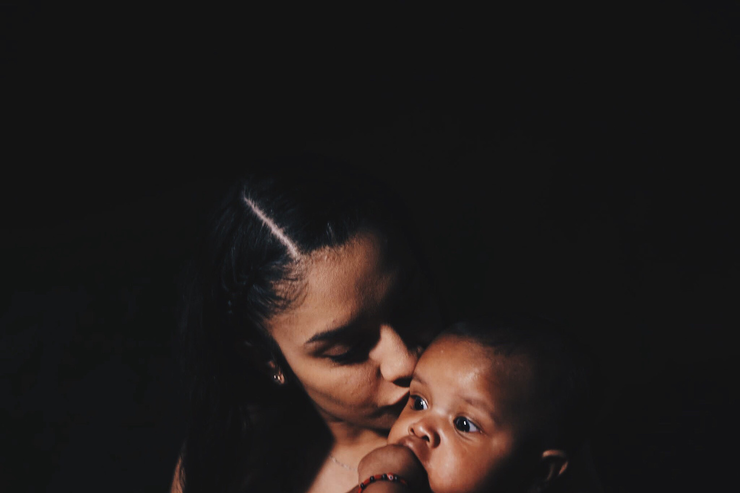 A Black mother holds her child and kisses them gently on the head.