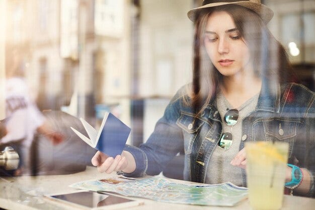 Turista sentado en un café leyendo un mapa con pasaporte bebiendo limonada en una ciudad ocupada Foto gratis