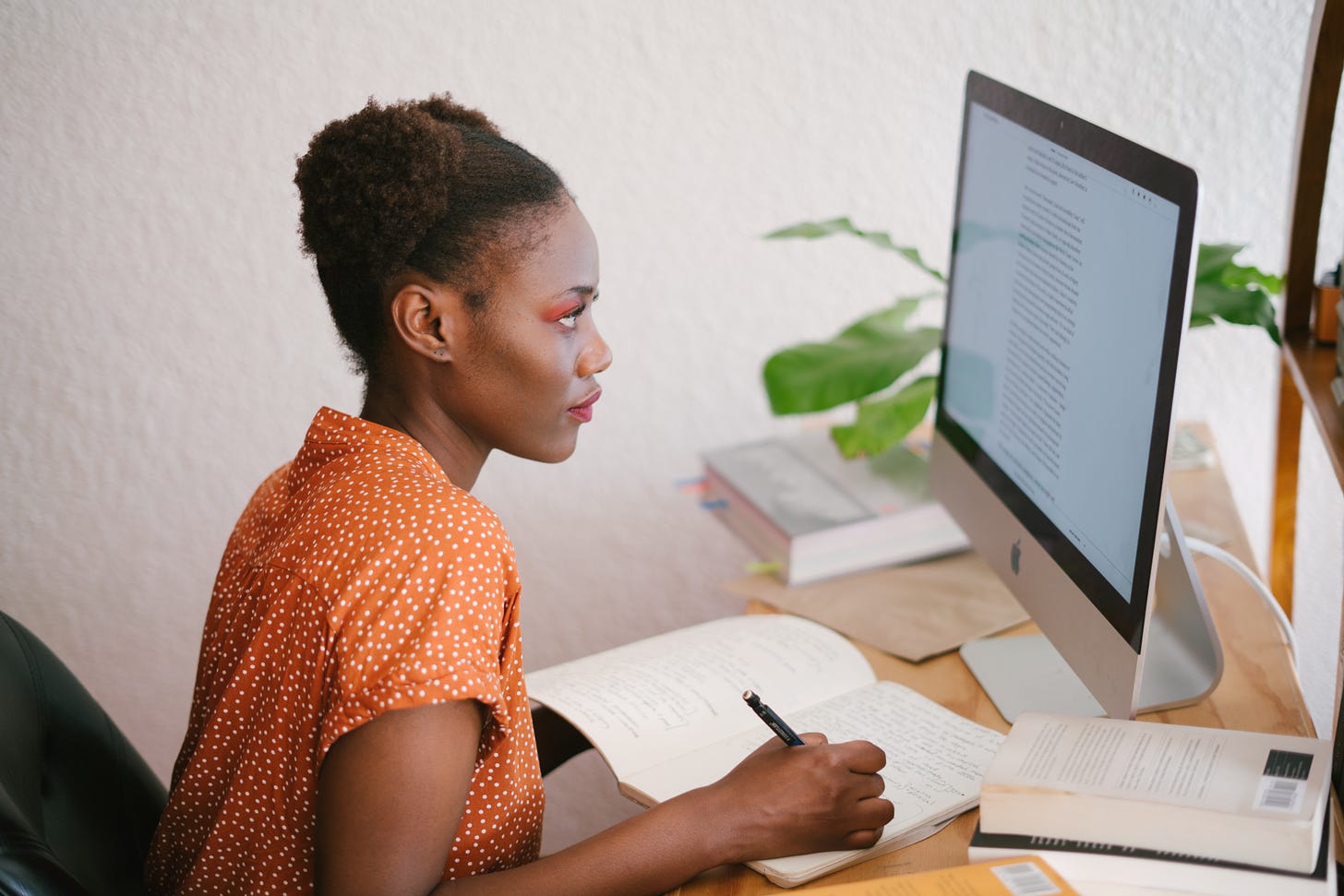 black woman looking at computer and writing in notebook