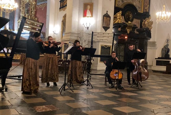 An orchestra playing in a grand church. There are ornate gold trims around paintings. 