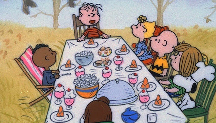 A still from A Charlie Brown Thanksgiving with the characters sitting around a table full of food.