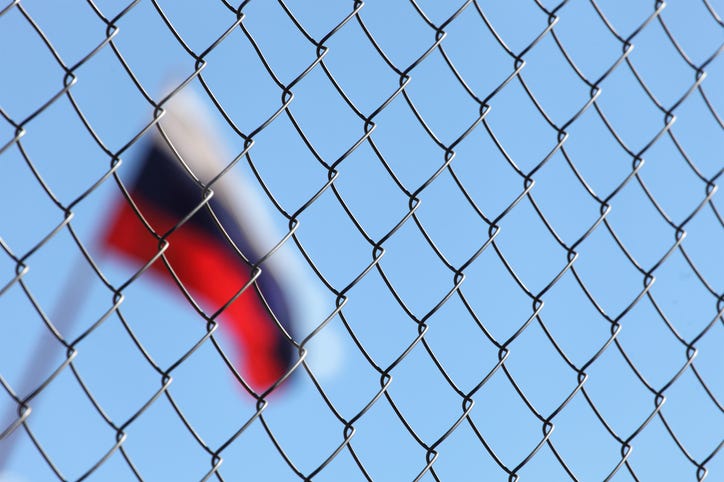 A Russian flag is positioned behind a chain link fence.
