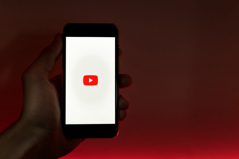 A man holding a phone with the Youtube logo on it.