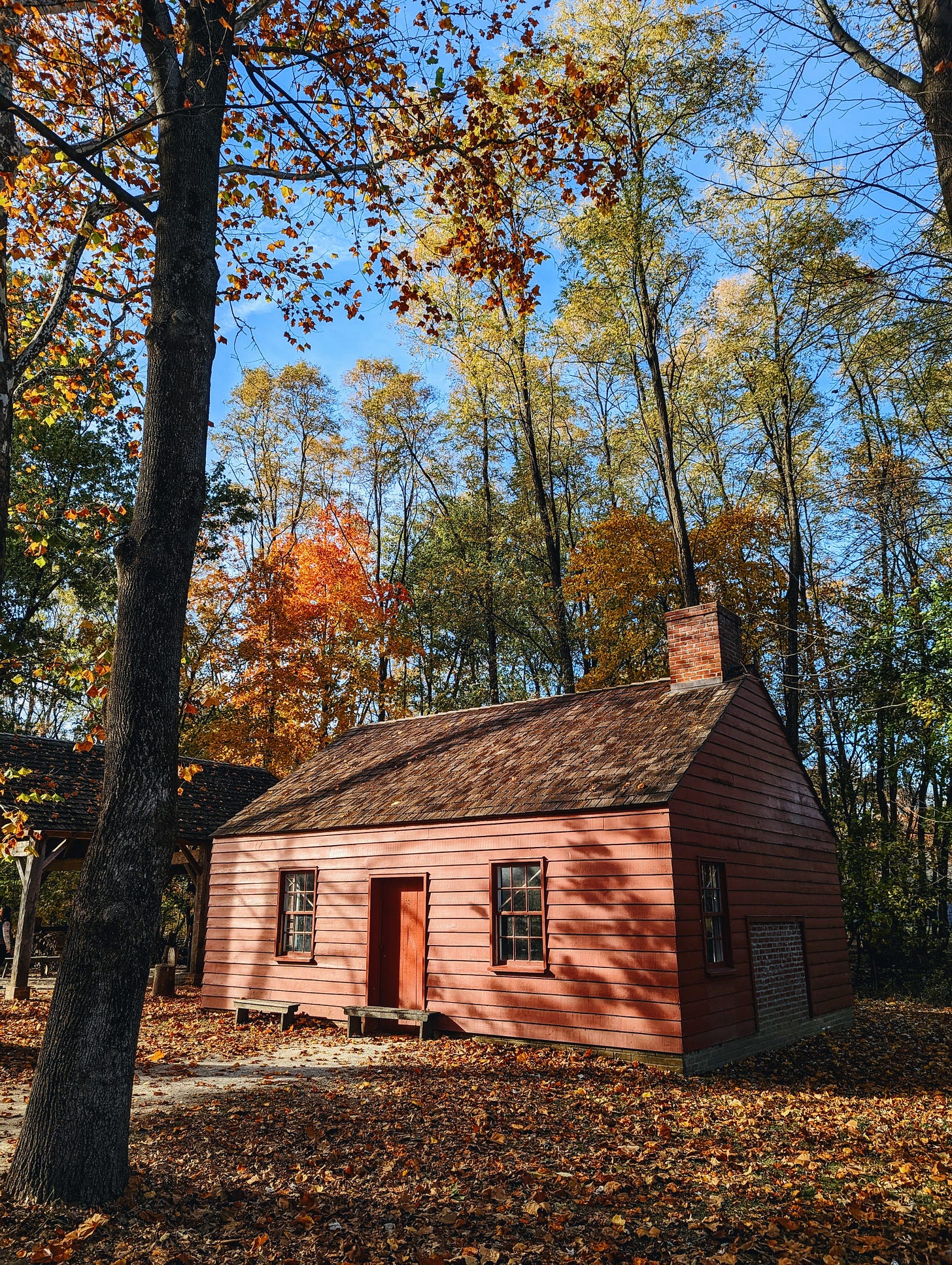 A charming red cabin sits among autumn leaves and trees in the fictional 1836 Prairie Town.