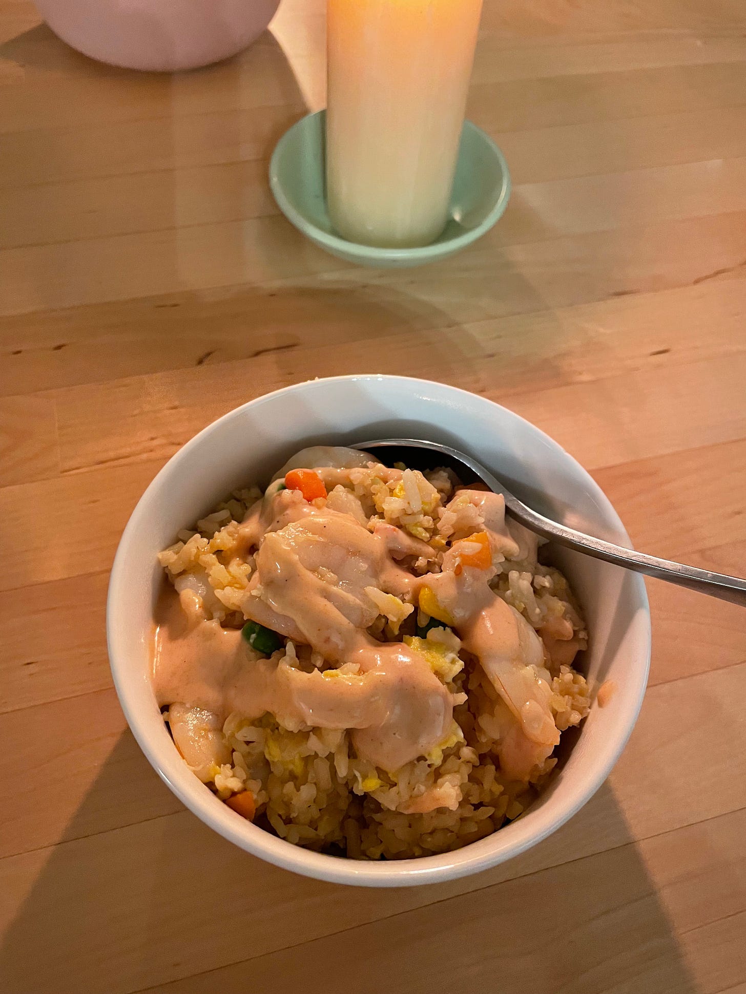 Bowl of prawn fried rice with drizzles of yum yum sauce on a dining table with candles