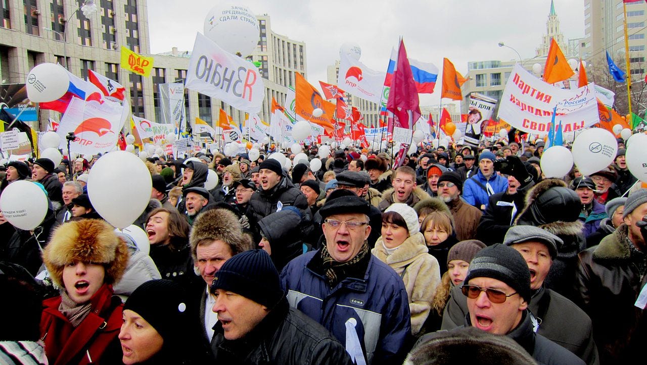 A crowd of enthusiastic protesters on Academician Sakharov Avenue, Moscow. Many balloons, posters, and flags. The protesters are bundled up on a cold overcast Winter day.
