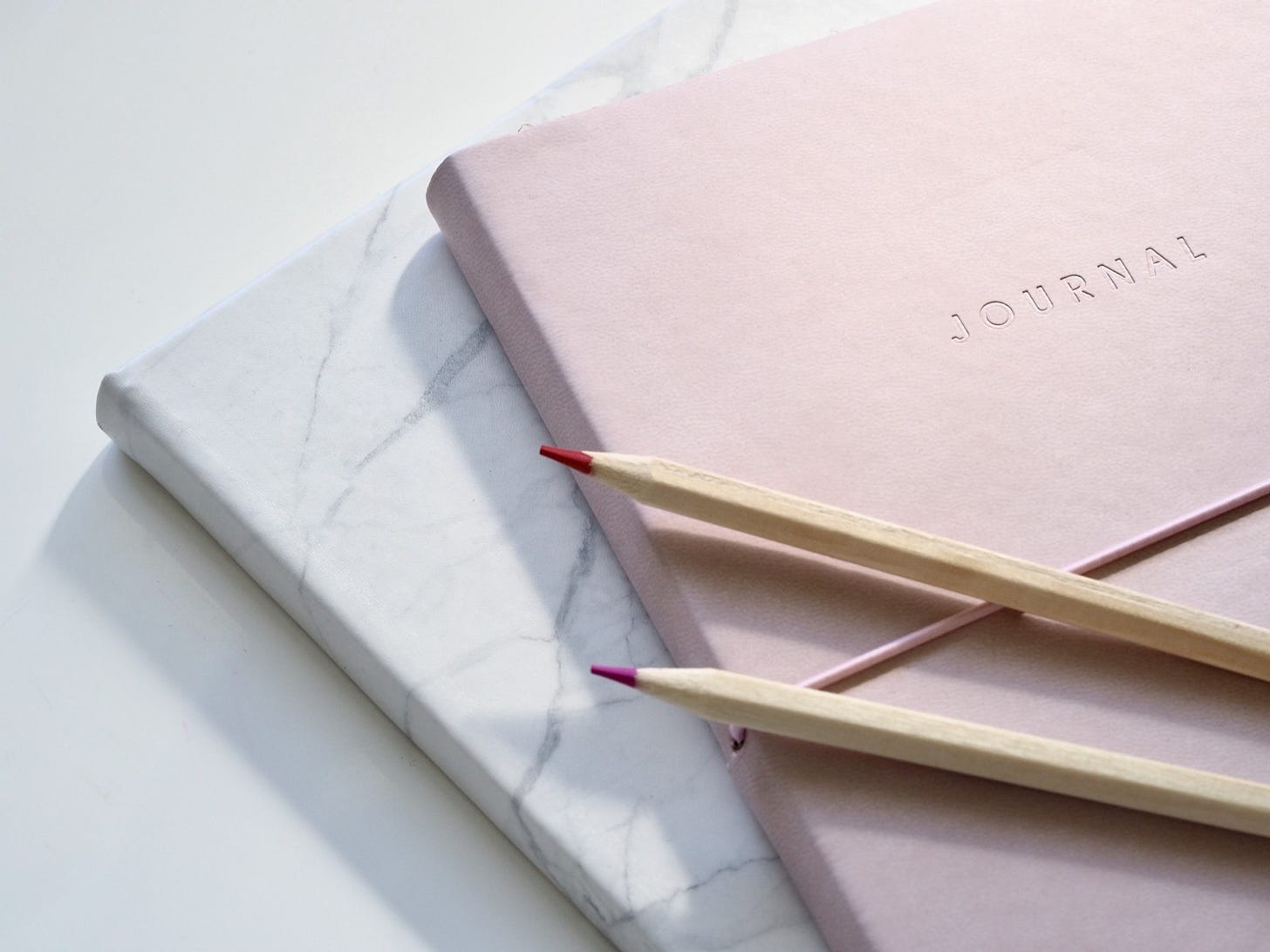 Pink journal and marble journal with two pencils to write morning pages.