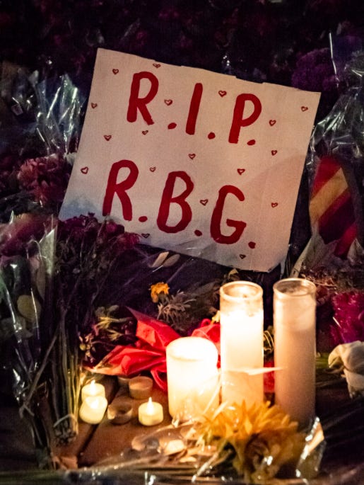 A poster with the words “R.I.P R.B.G” in front of a pile of candles and flowers.