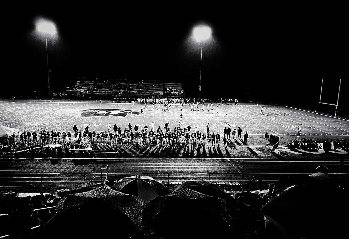A photograph of a rainy Friday night high school American football game taken from the top row of the stadium.