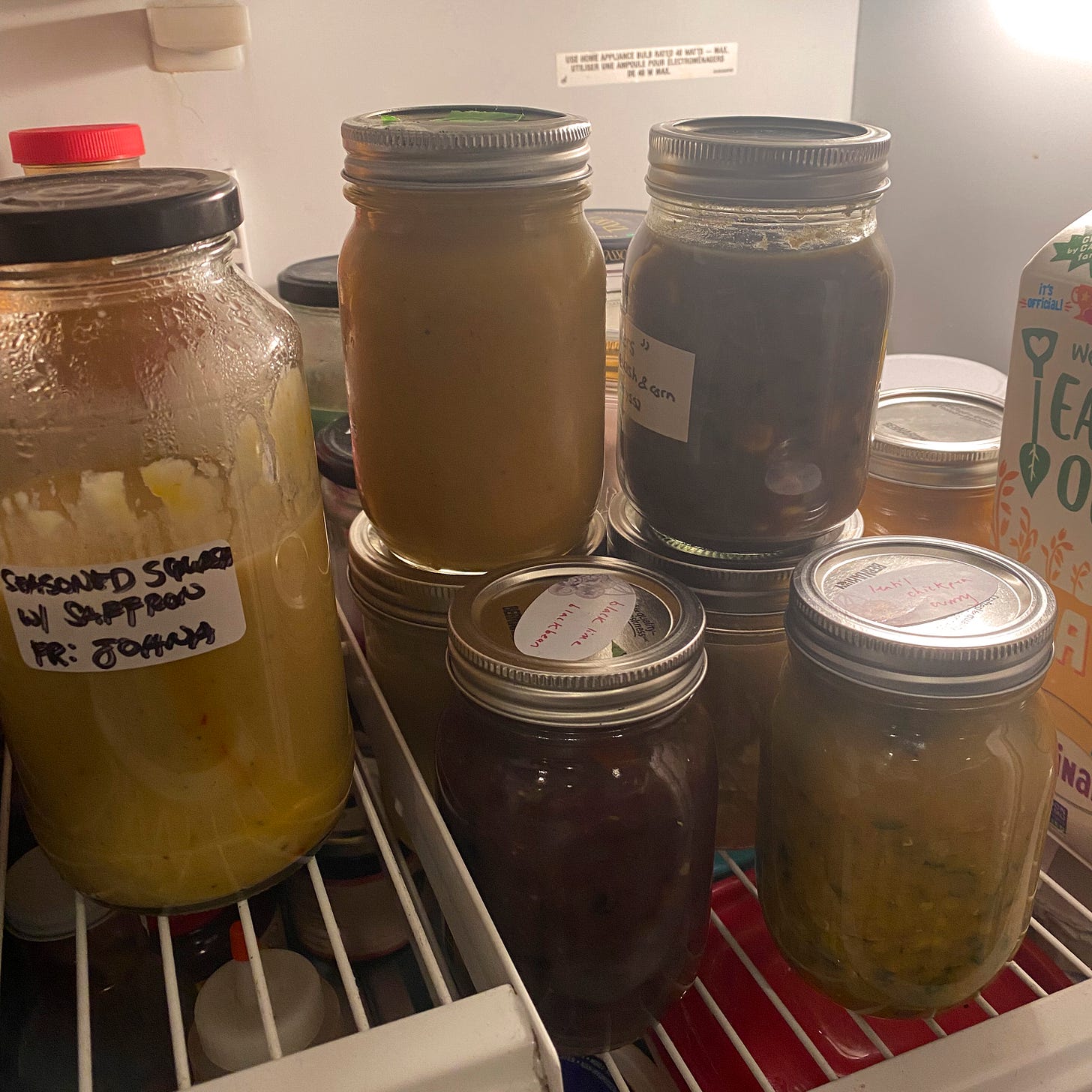 Several jars of various different soups on the top shelf of a fridge.
