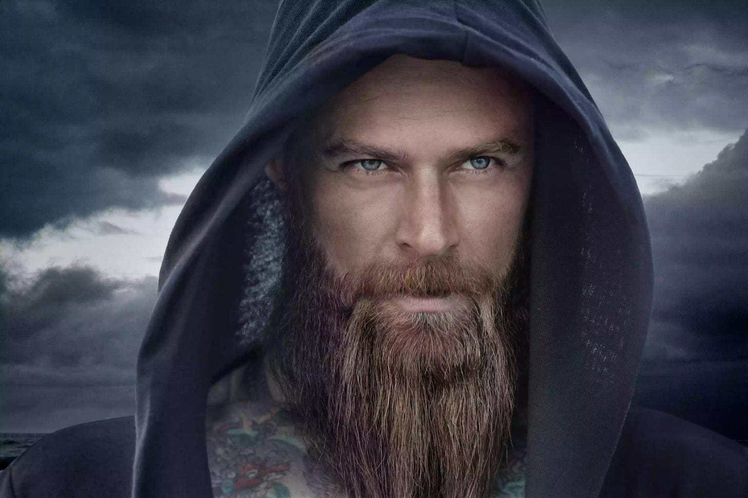 Hooded bearded tattooed male in fantasy cloudy seascape setting