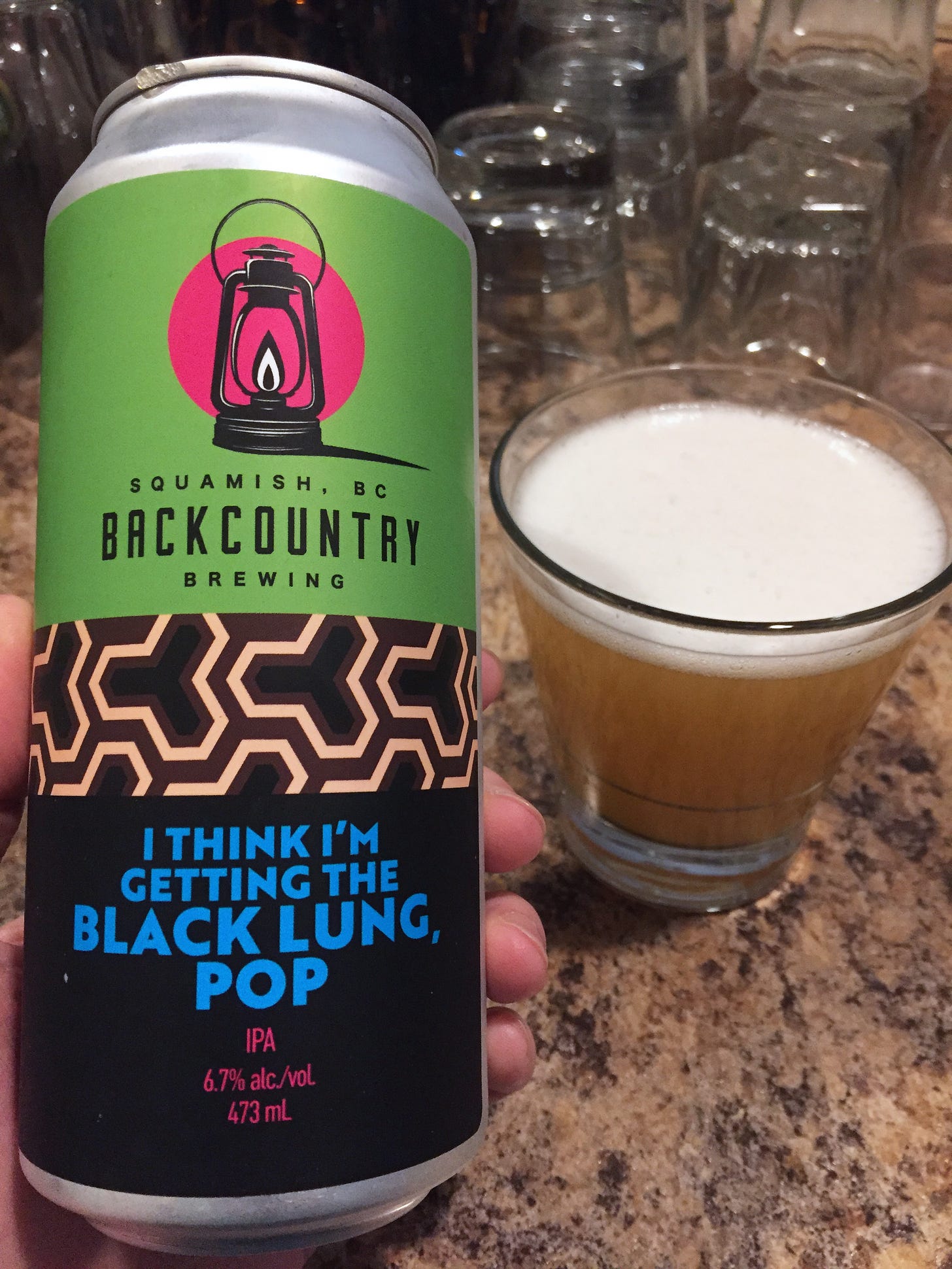 a black, green, and pink beer can from Backcountry Brewing with blue text that reads, "I think I'm getting the black lung, Pop" in all caps. A glass of the beer is in the background.