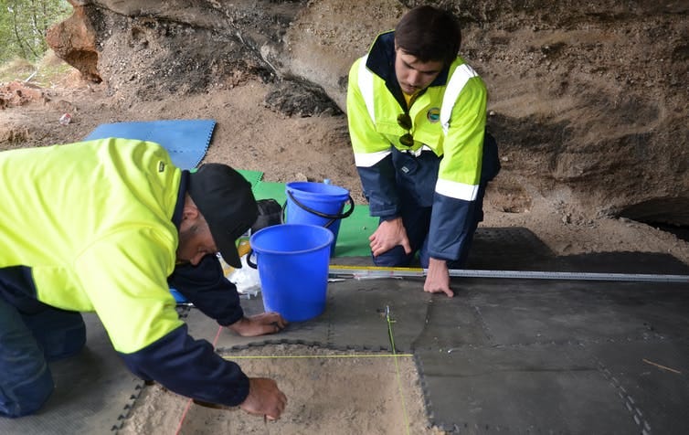 Two people excavating the ground of a rockshelter.